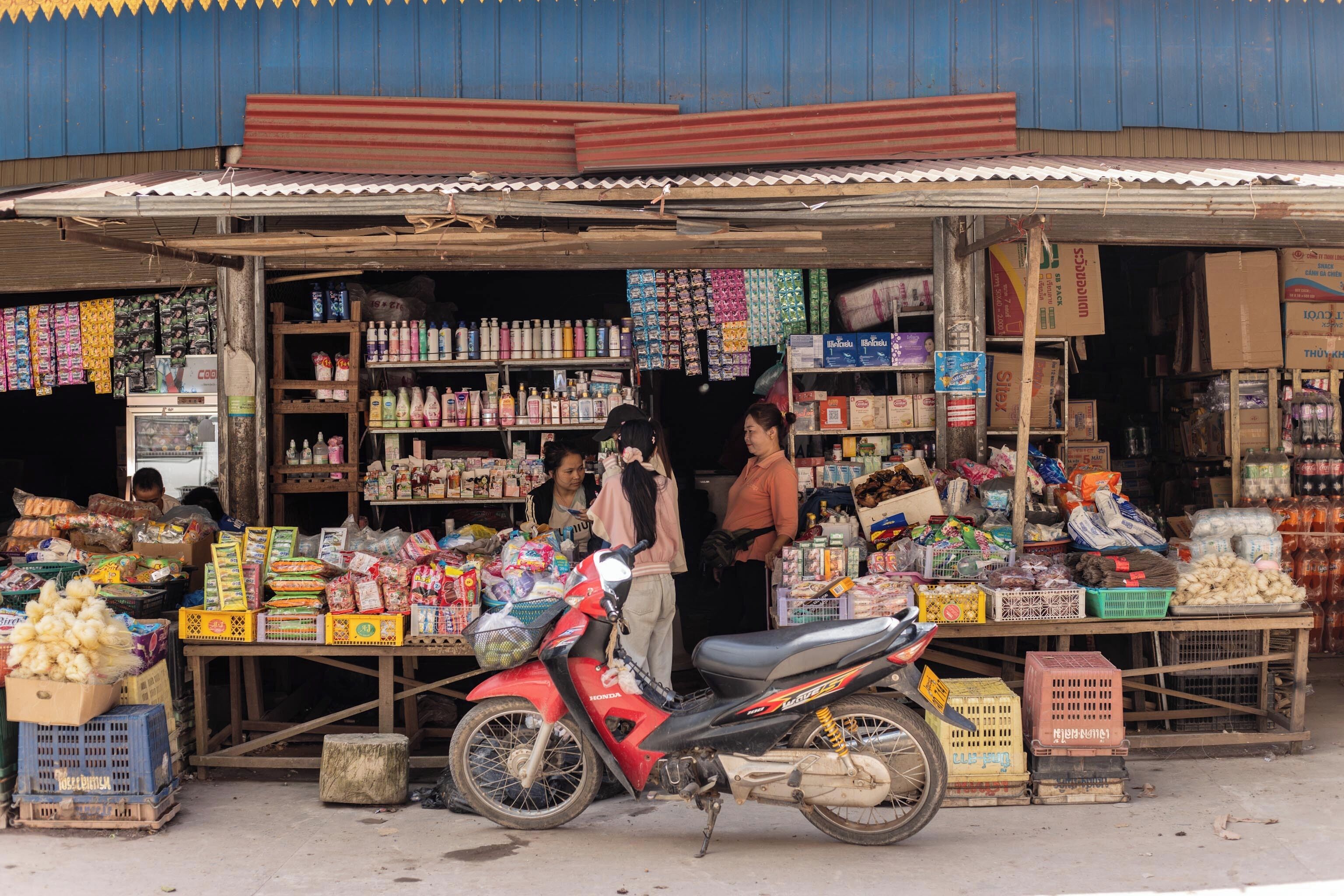 Un pequeño puesto de mercado con diversos productos y una motocicleta estacionada al frente.