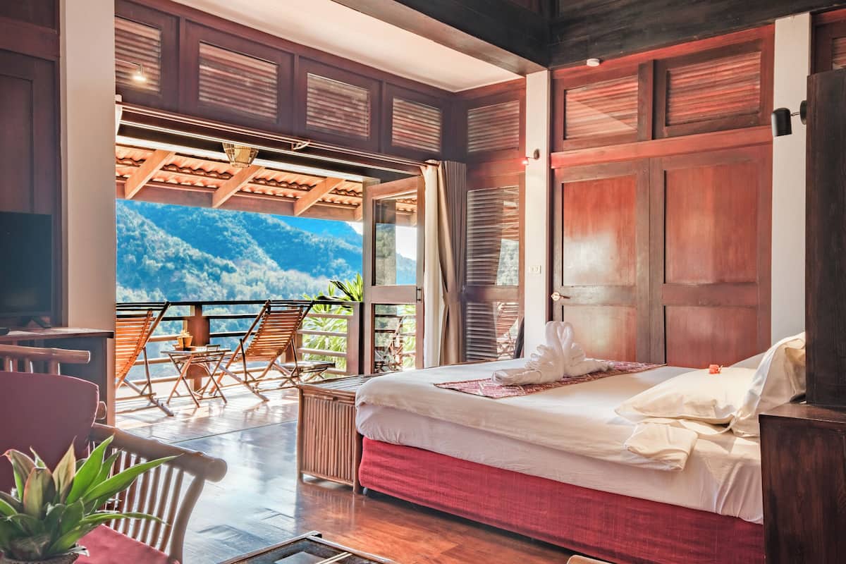 A bedroom with a large bed, wooden furniture, and a view of mountains through an open door.