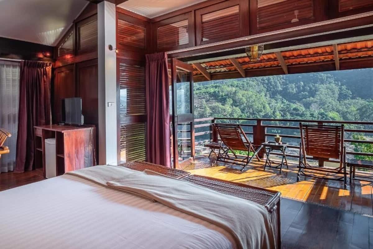 A bedroom with a large bed, a desk with a television, and a balcony with chairs and a table.