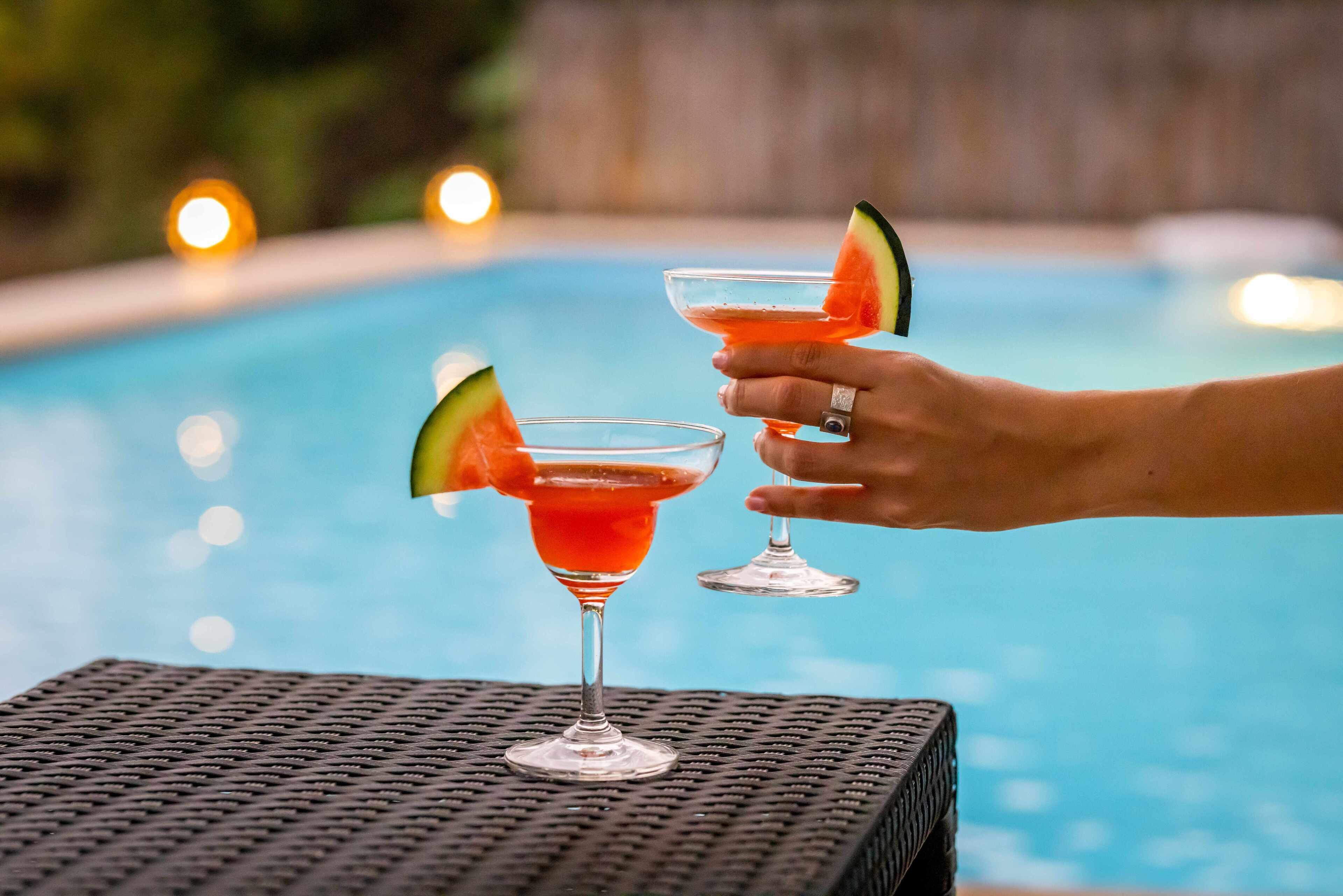 Deux cocktails décorés de tranches de pastèque, posés sur une table au bord d’une piscine.