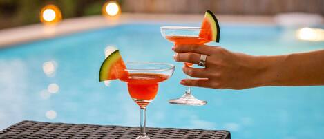 Two cocktails with watermelon garnish on a table by a pool.