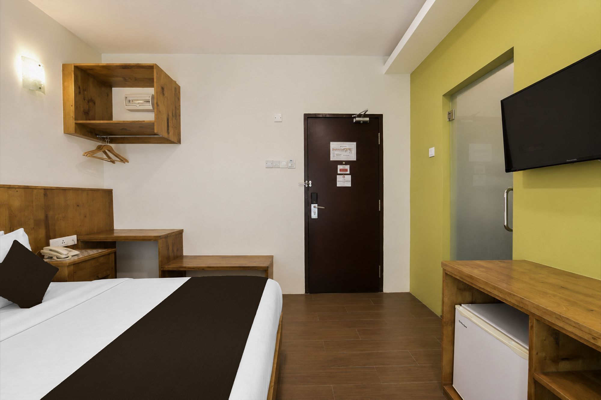 Une chambre d’hôtel comprenant un lit, une table de chevet, un bureau, un petit réfrigérateur, un téléviseur fixé au mur et une porte avec une pancarte.