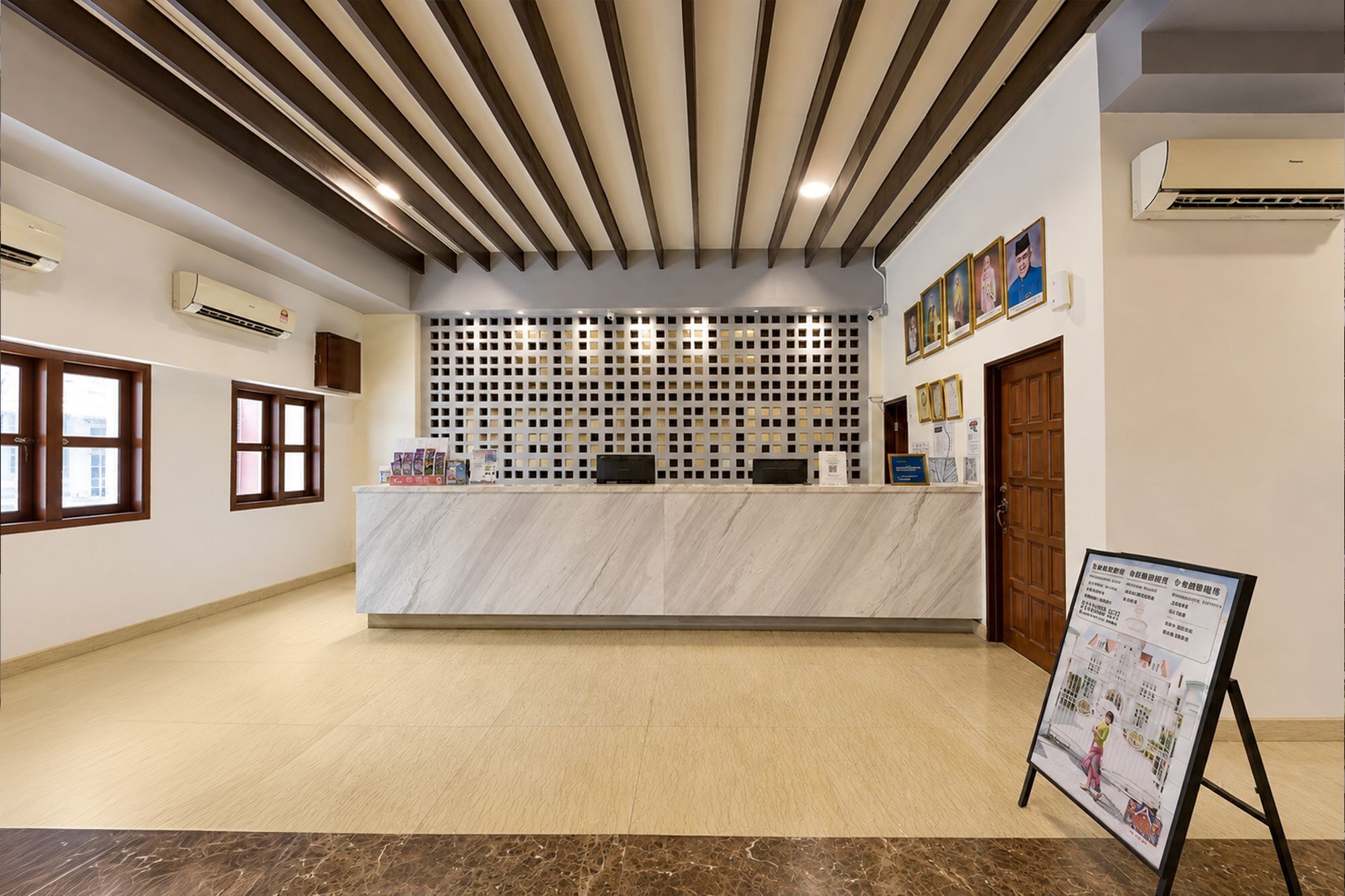 A reception area with a marble counter, wooden ceiling beams, air conditioning units, and framed pictures on the wall.