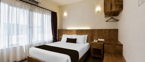 Habitación de hotel con una cama de madera, una mesita de noche, un perchero de madera y un equipo de aire acondicionado.