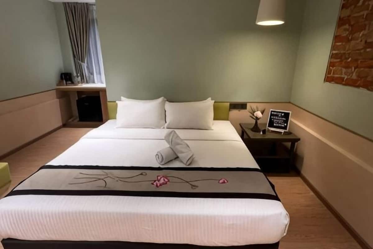 Une chambre d’hôtel avec un lit, une table de chevet, une lampe et une fenêtre avec des rideaux.