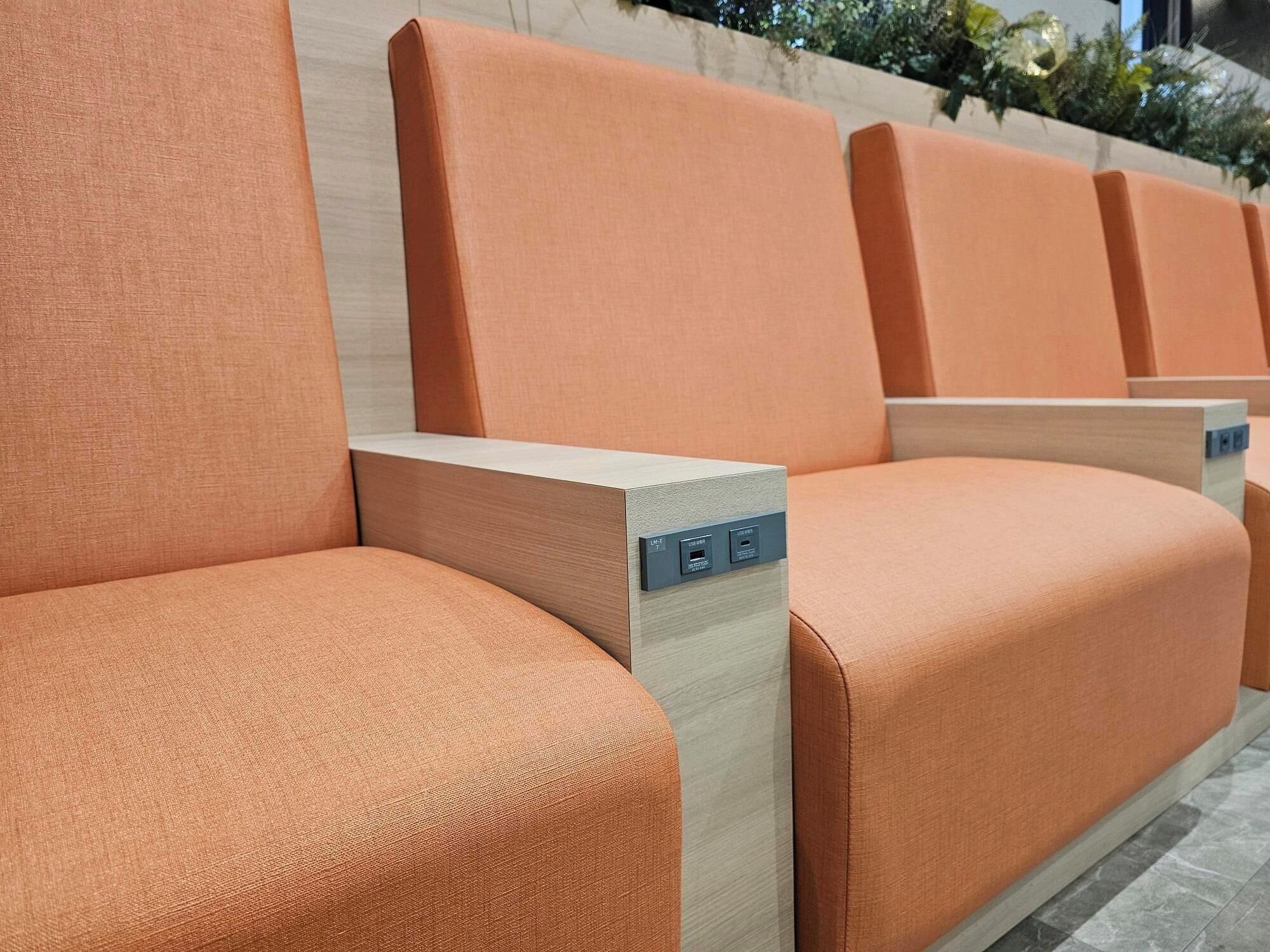 A row of orange upholstered chairs with wooden armrests and a light-colored floor.