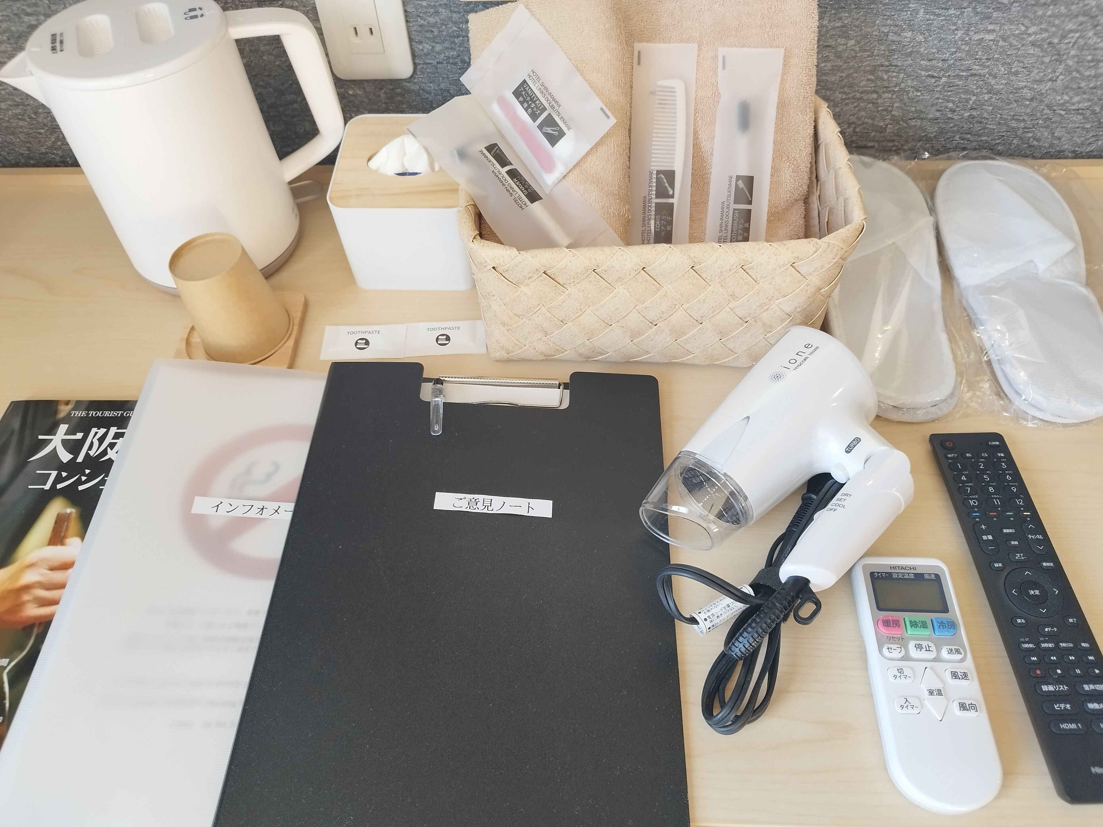 A neatly organized workspace with a black clipboard, a white hairdryer, a black remote control, and a white kettle.
