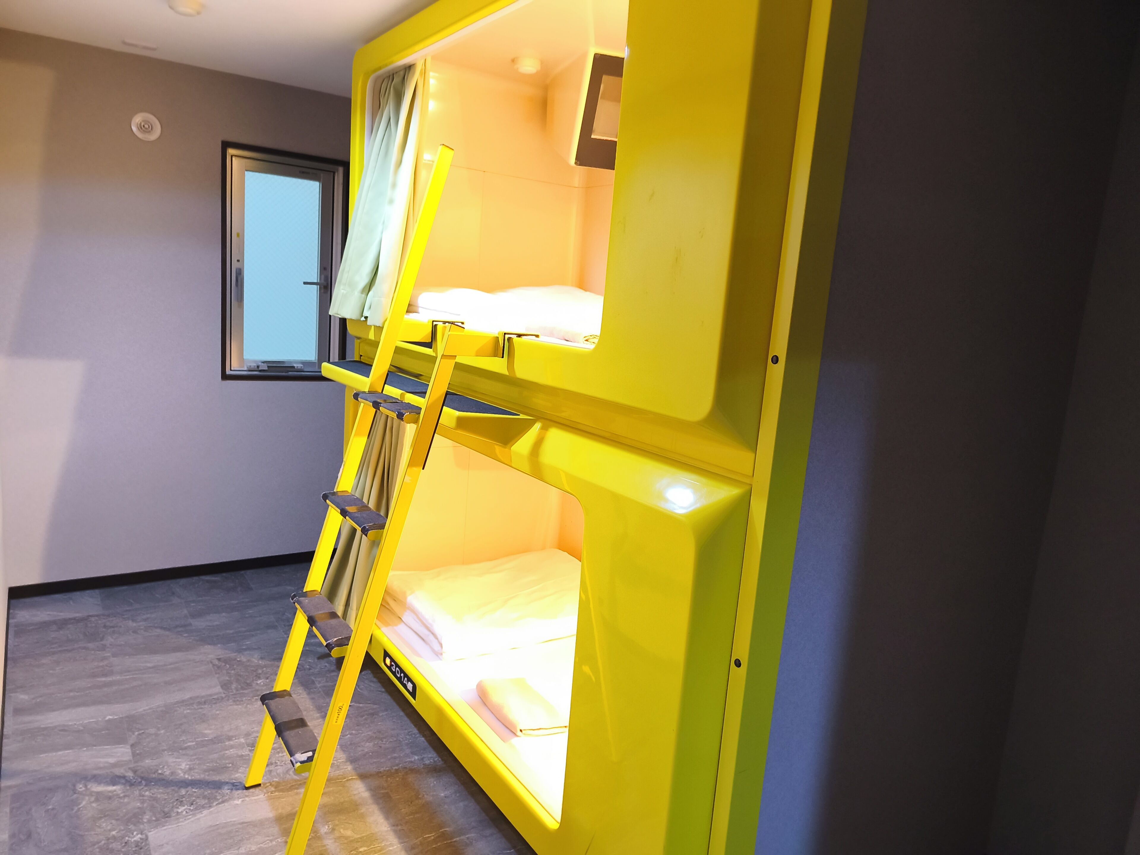 A bunk bed with a ladder, a window, and a bed with pillows.