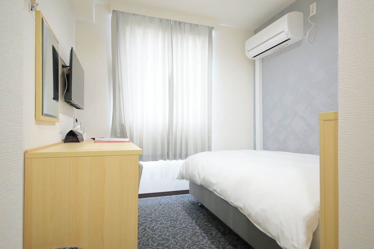 Una habitación de hotel con una cama, un escritorio, un televisor y un equipo de aire acondicionado.