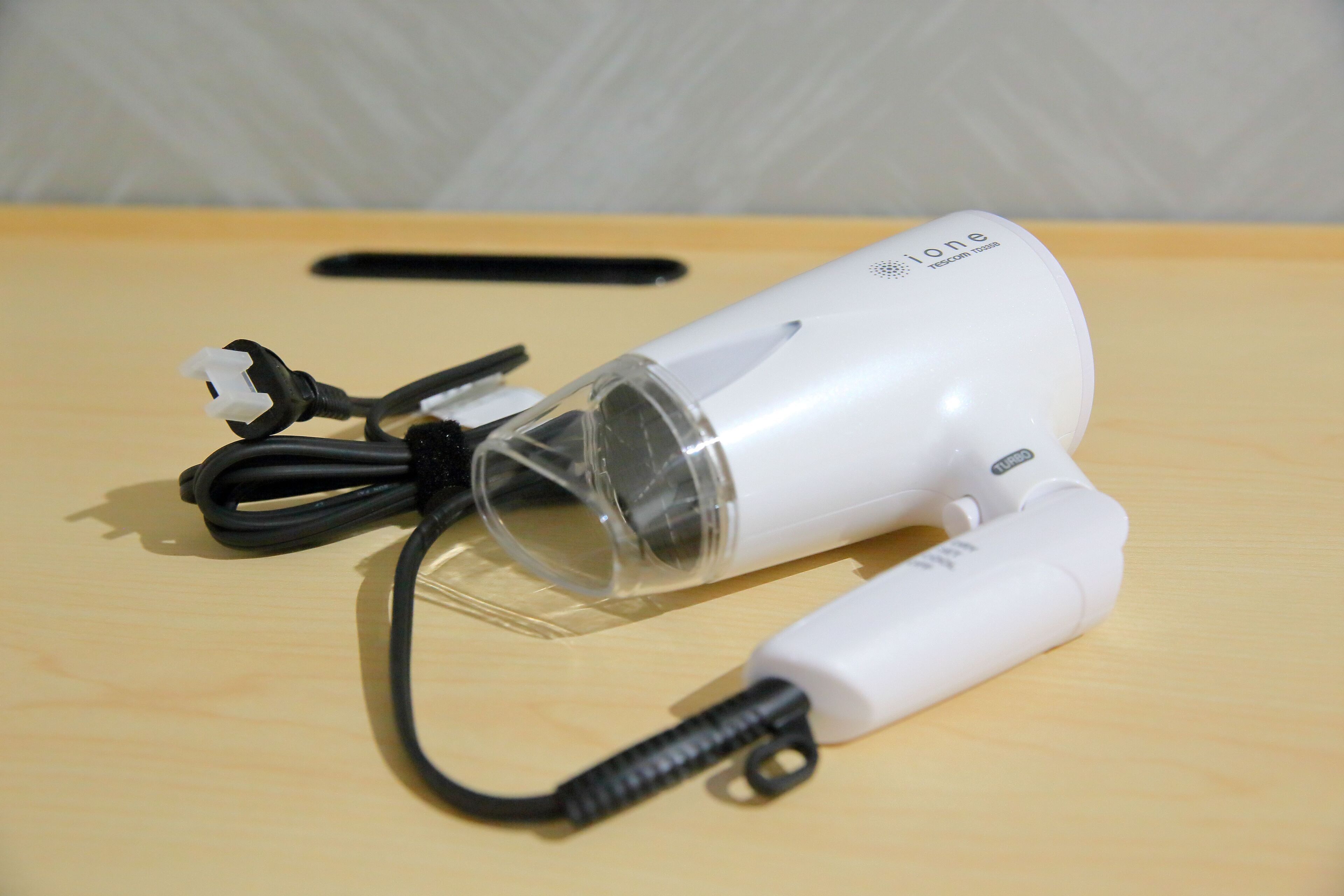 A white hair dryer with a transparent water bottle attached, lying on a wooden surface.