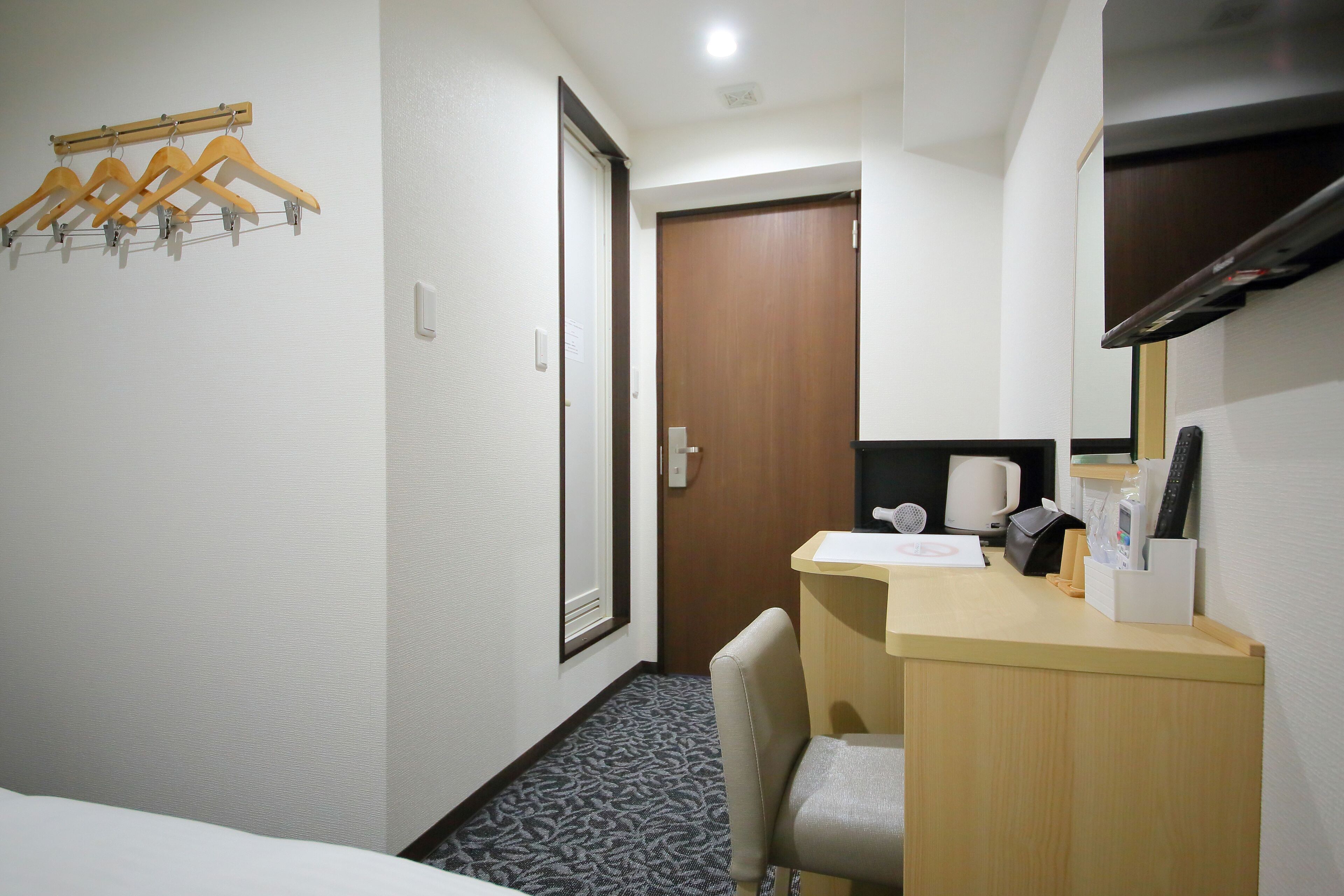 Une chambre d’hôtel comprenant un lit, un bureau avec une chaise, un porte-manteau en bois et une porte.