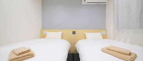 Et hotelværelse med to senge, hver med et pænt foldet beige håndklæde.