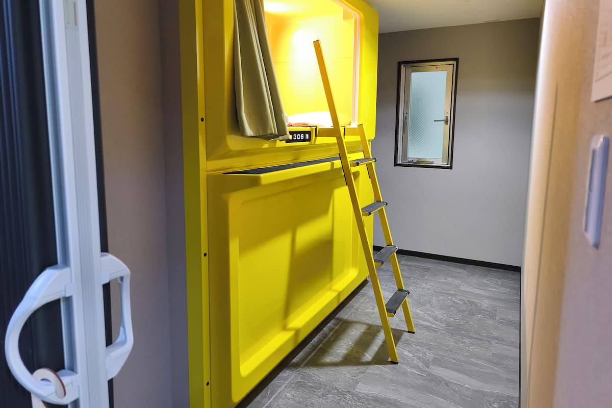 Una habitación con un armario amarillo, una escalera y un ventanal.