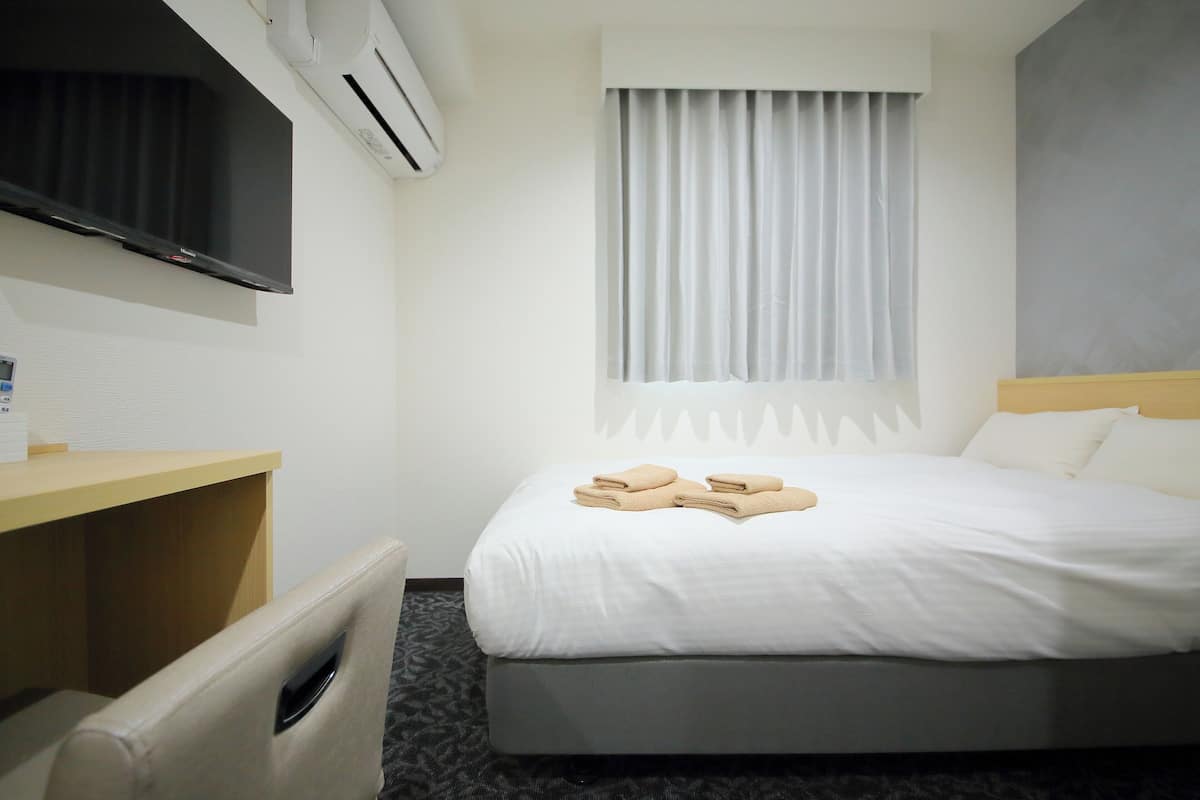 Una habitación de hotel con cama, escritorio, televisión y ventana con cortinas.