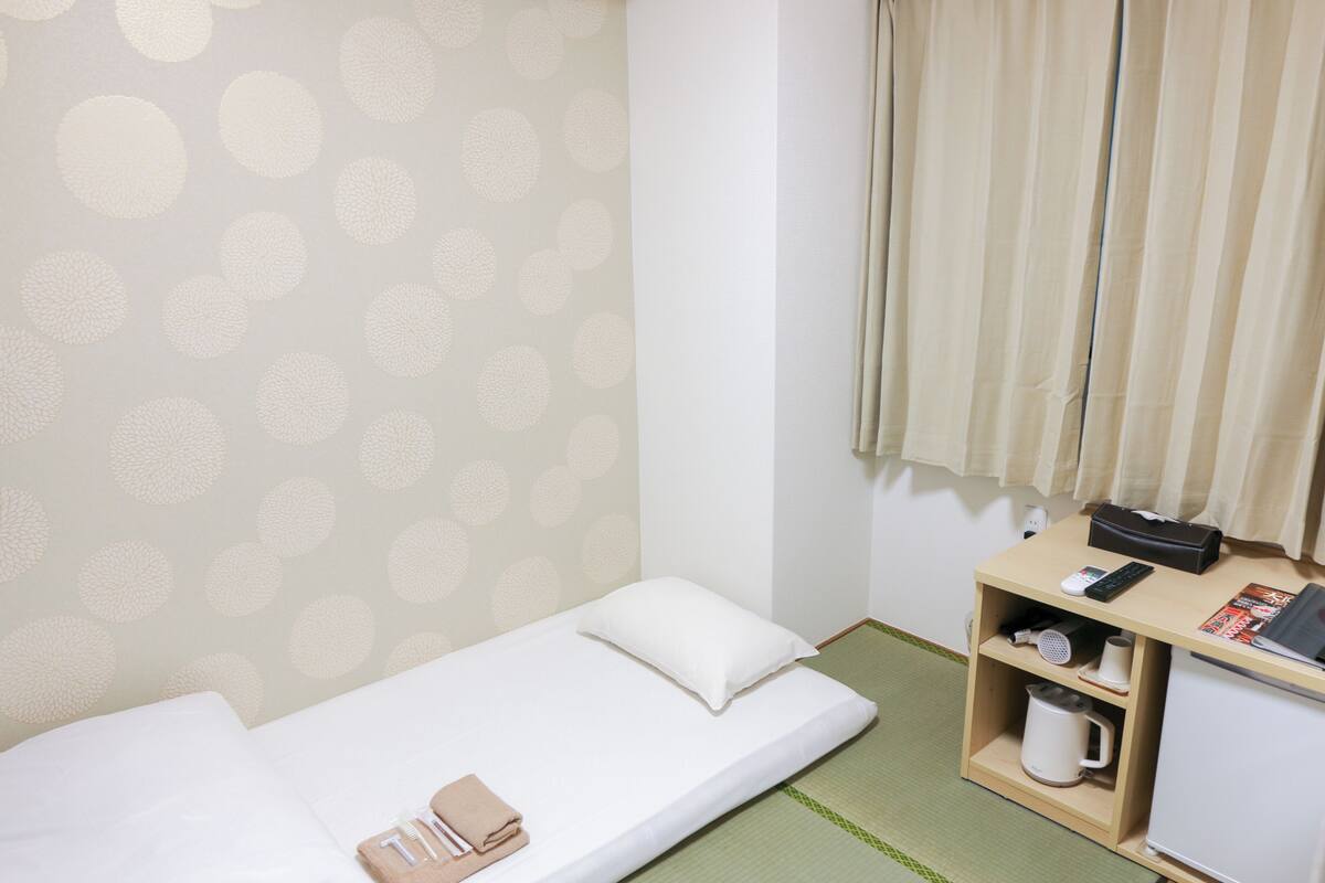 Habitación individual con papel tapiz de lunares, una estantería pequeña con una tetera, un mando a distancia y una revista.