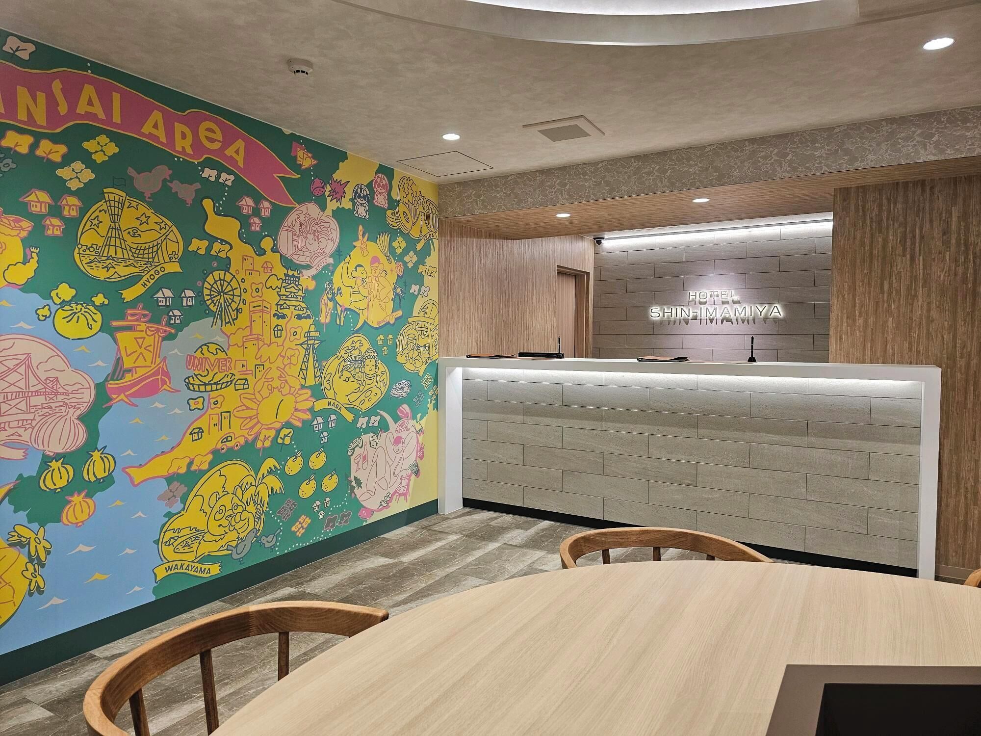 A hotel reception area with a colorful mural, a reception desk, and a seating area with wooden chairs.