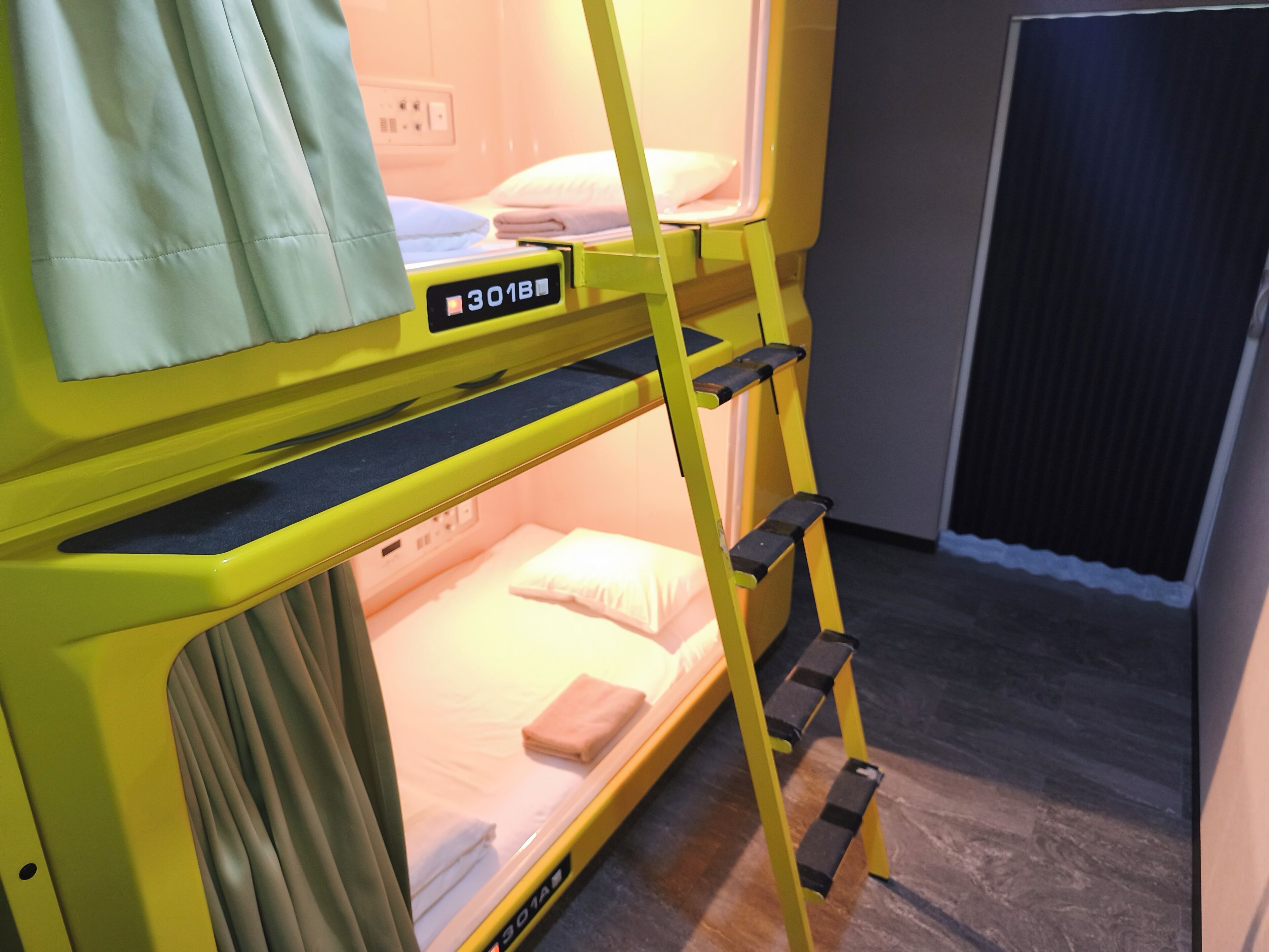 Un lit superposé avec une structure jaune, un petit bureau et une fenêtre.