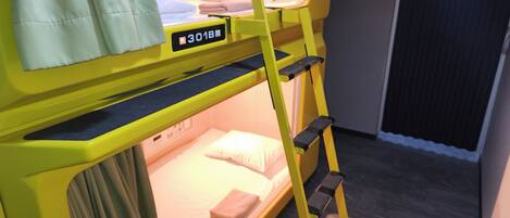 Un lit superposé avec une structure jaune, un petit bureau et une fenêtre.