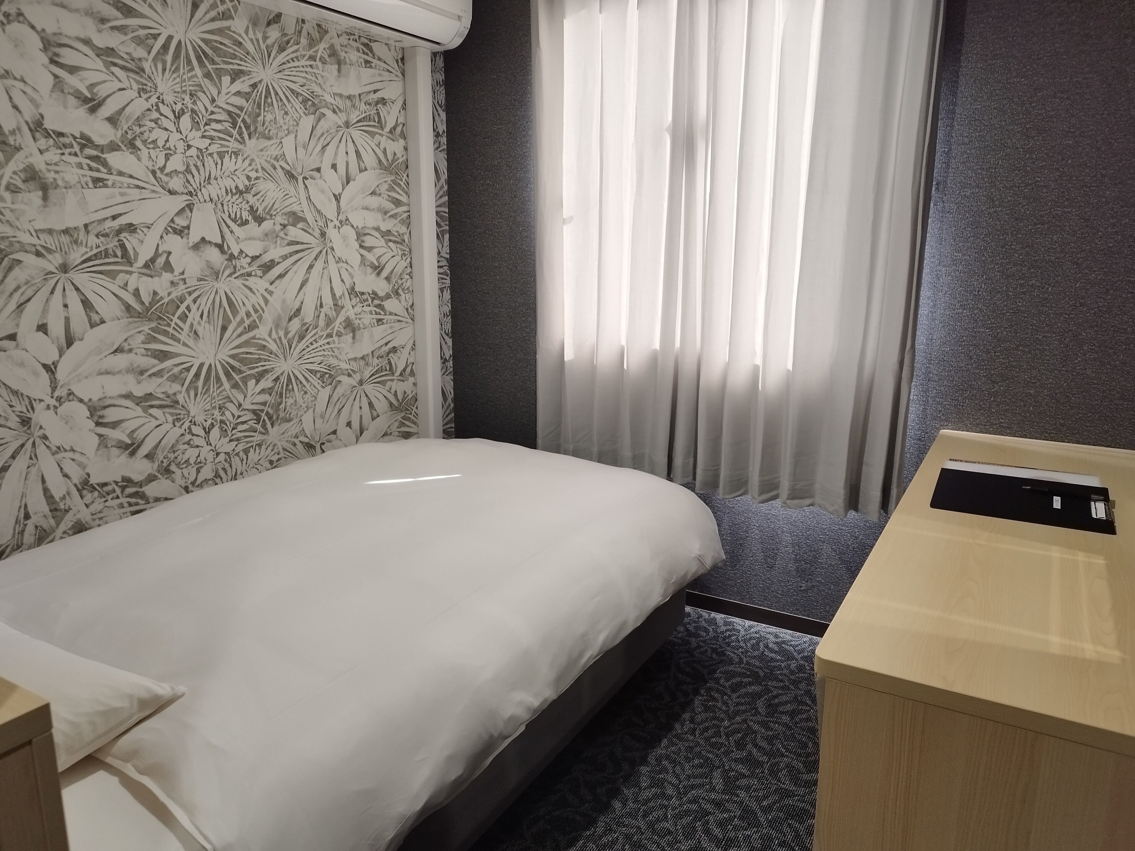 A hotel room with a bed, a nightstand, a desk, and a window with curtains.