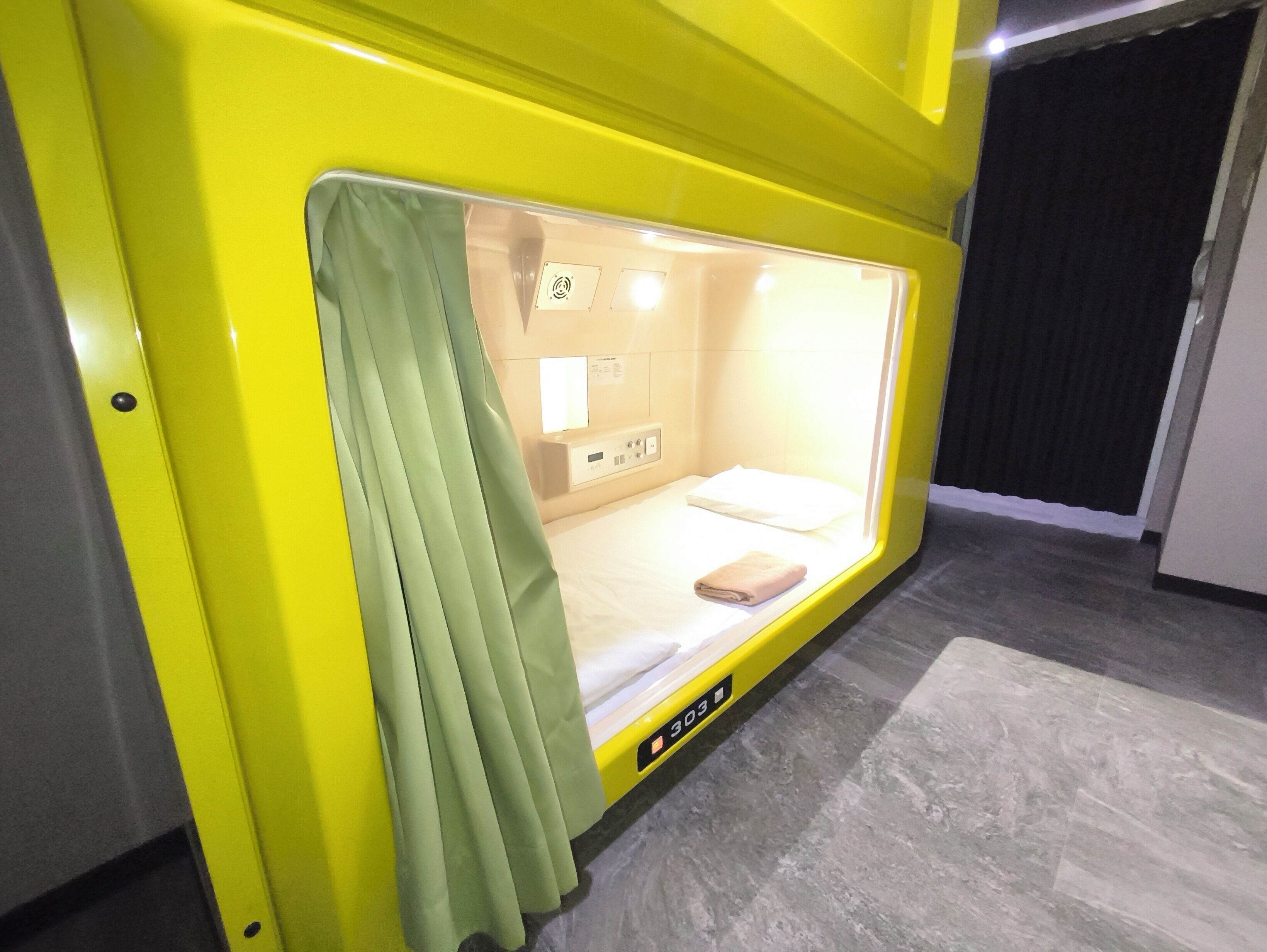 Una habitación pequeña y luminosa con una cama individual, una mesita de noche y una cortina.