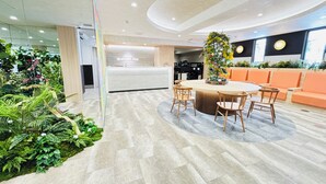A modern reception area with a reception desk, a round table with chairs, and a seating area with orange sofas. - Shin-Imamiya Hotel (Osaka)