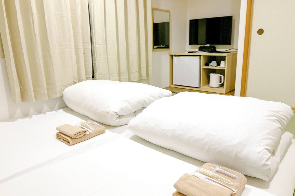 Habitación de hotel con dos camas, un escritorio pequeño con espejo, televisor y cafetera.