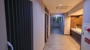 A hotel corridor with a wooden floor, a reception desk with a red emergency button, and a window with blinds. - Shin-Imamiya Hotel (Osaka)