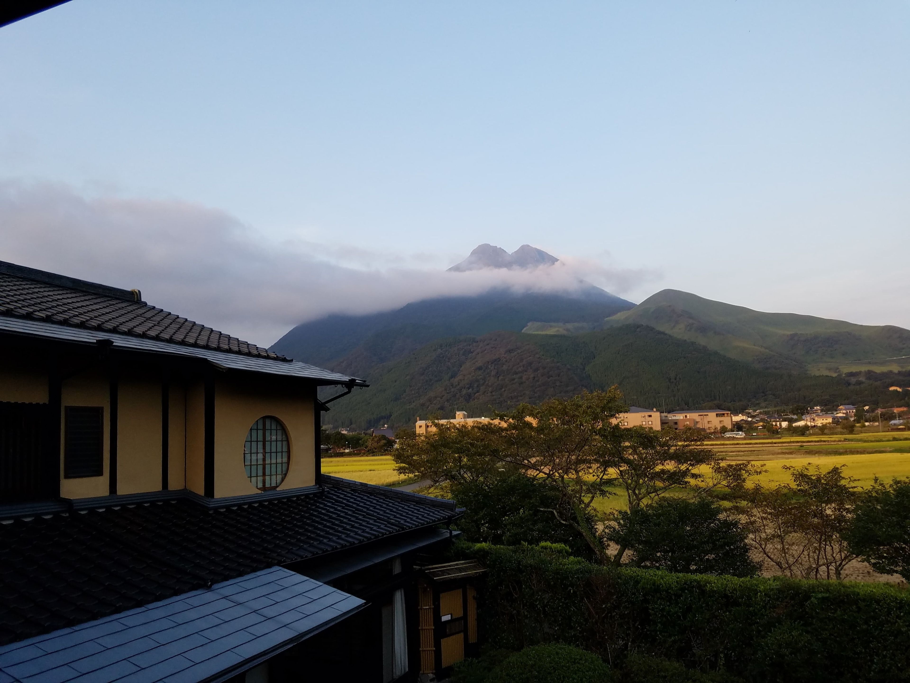 A traditional building with a tiled roof, surrounded by lush greenery and a mountainous landscape.