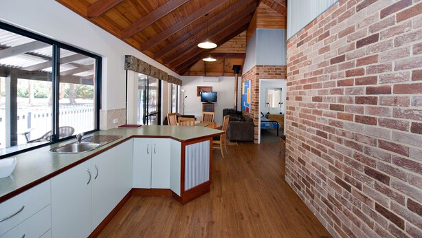 A modern kitchen with a wooden ceiling, a brick wall, and a large window. - Margaret River Hideaway (Bramley)