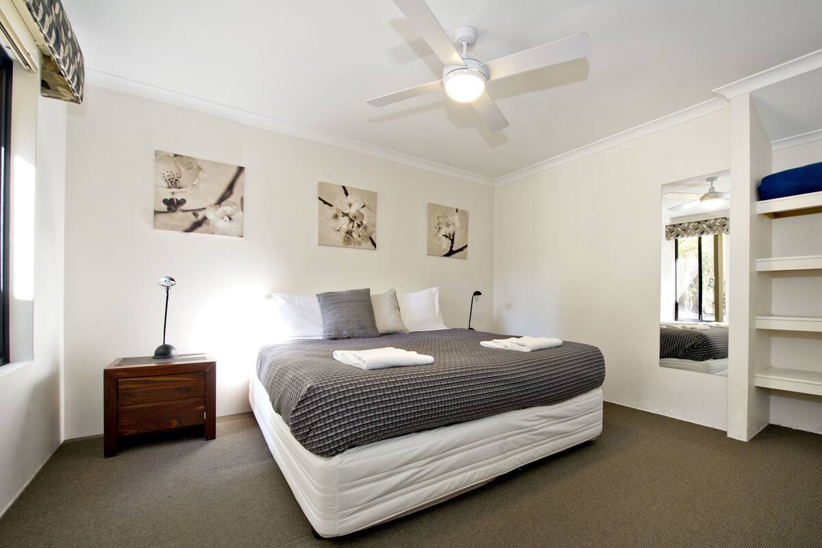 A bedroom with a bed, a nightstand, a ceiling fan, and artwork on the walls.