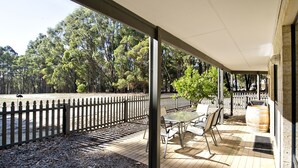 An outdoor patio with a table and chairs, a wooden fence, and a view of a forested area. - Margaret River Hideaway (Bramley)
