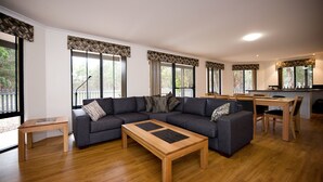 A modern living room with a sectional sofa, a wooden coffee table, and a dining area with a wooden table and chairs. - Margaret River Hideaway (Bramley)