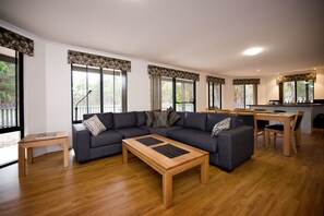 Una sala de estar moderna con un sofá seccional, una mesa de centro de madera y un comedor con una mesa y sillas de madera.