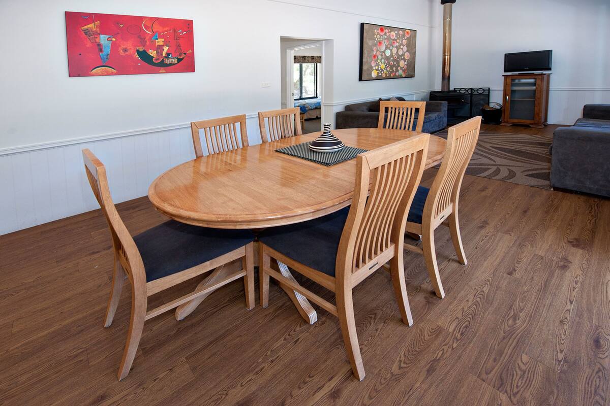 A dining area with a round wooden table and six chairs, a sofa, and a television in the background.