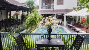 A balcony with a table and chairs, a pool, and lounge chairs. - Starfruit Villa Hoi An (Da Nang)