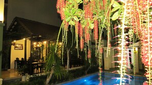 An outdoor pool area with hanging floral decorations, a dining area with tables and chairs, and a building with a sloped roof. - Starfruit Villa Hoi An (Da Nang)
