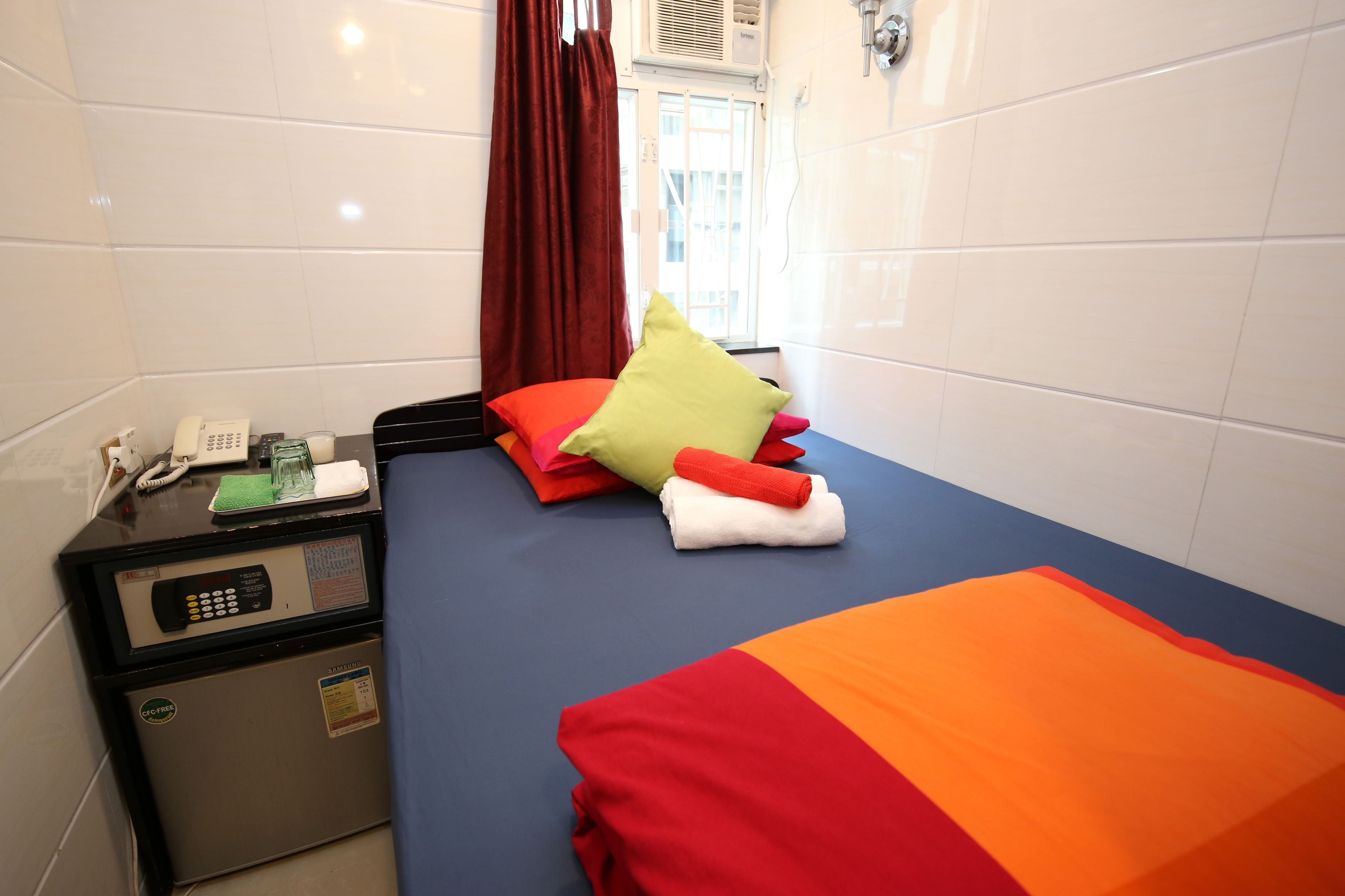 A small hotel room with a bed, a desk with a phone, and a mini-fridge.