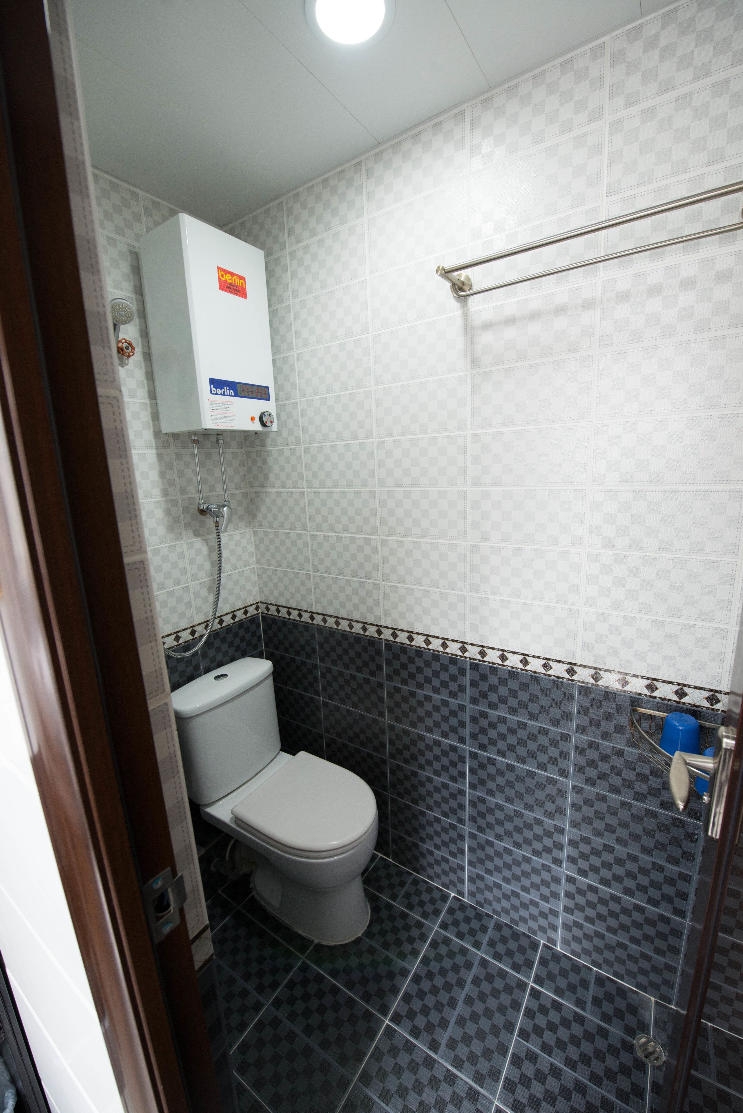 A bathroom with a toilet, a wall-mounted water heater, and a shower area.