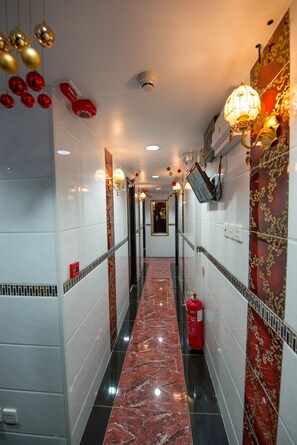 Un couloir au sol en marbre, agrémenté de luminaires fixés aux murs et de décorations rouges et dorées.