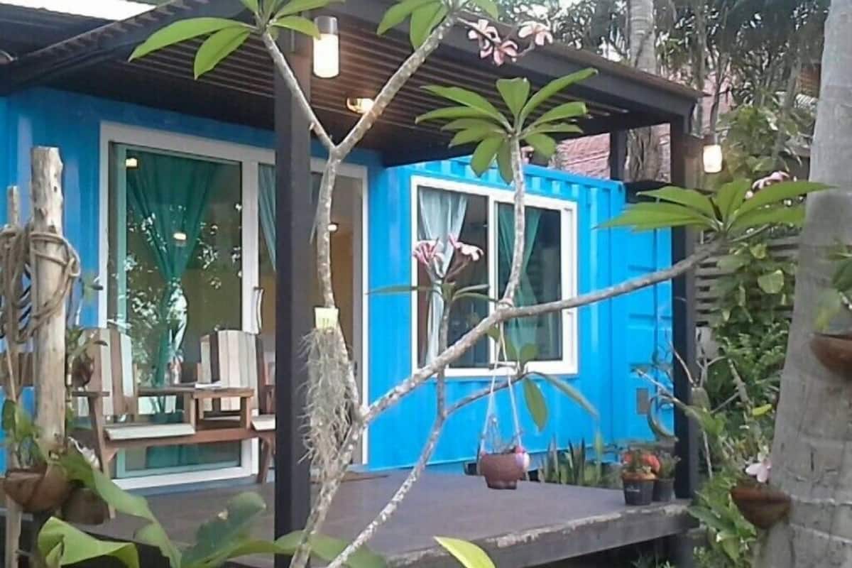 A blue house with a porch, surrounded by greenery and potted plants.