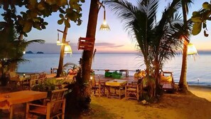 A beachside restaurant with wooden tables and chairs, palm trees, and a view of the sea at sunset. - Think & Retro Cafe Lipa Noi Samui (Koh Samui)