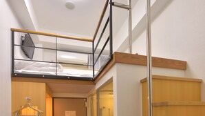 Habitación de hotel compacta con cama tipo altiloja, un escritorio con silla, baño pequeño y una escalera.