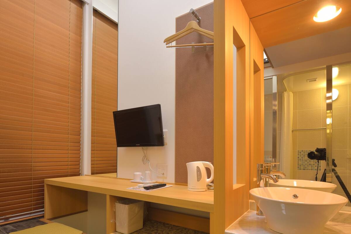 Ein modernes Badezimmer mit einem Holz-Waschtisch, einem großen Spiegel, einem Waschbecken und einem an der Wand befestigten Fernseher.