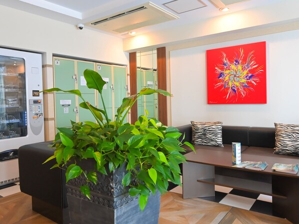 Un área de recepción con una planta, un sofá, una mesa y un cuadro abstracto colorido.