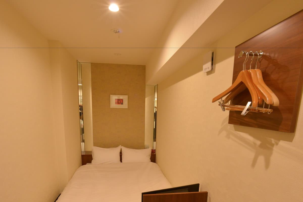 Ein Hotelzimmer mit einem Bett, einer hölzernen Bank, einem Wandhaken und einem kleinen gerahmten Bild an der Wand.