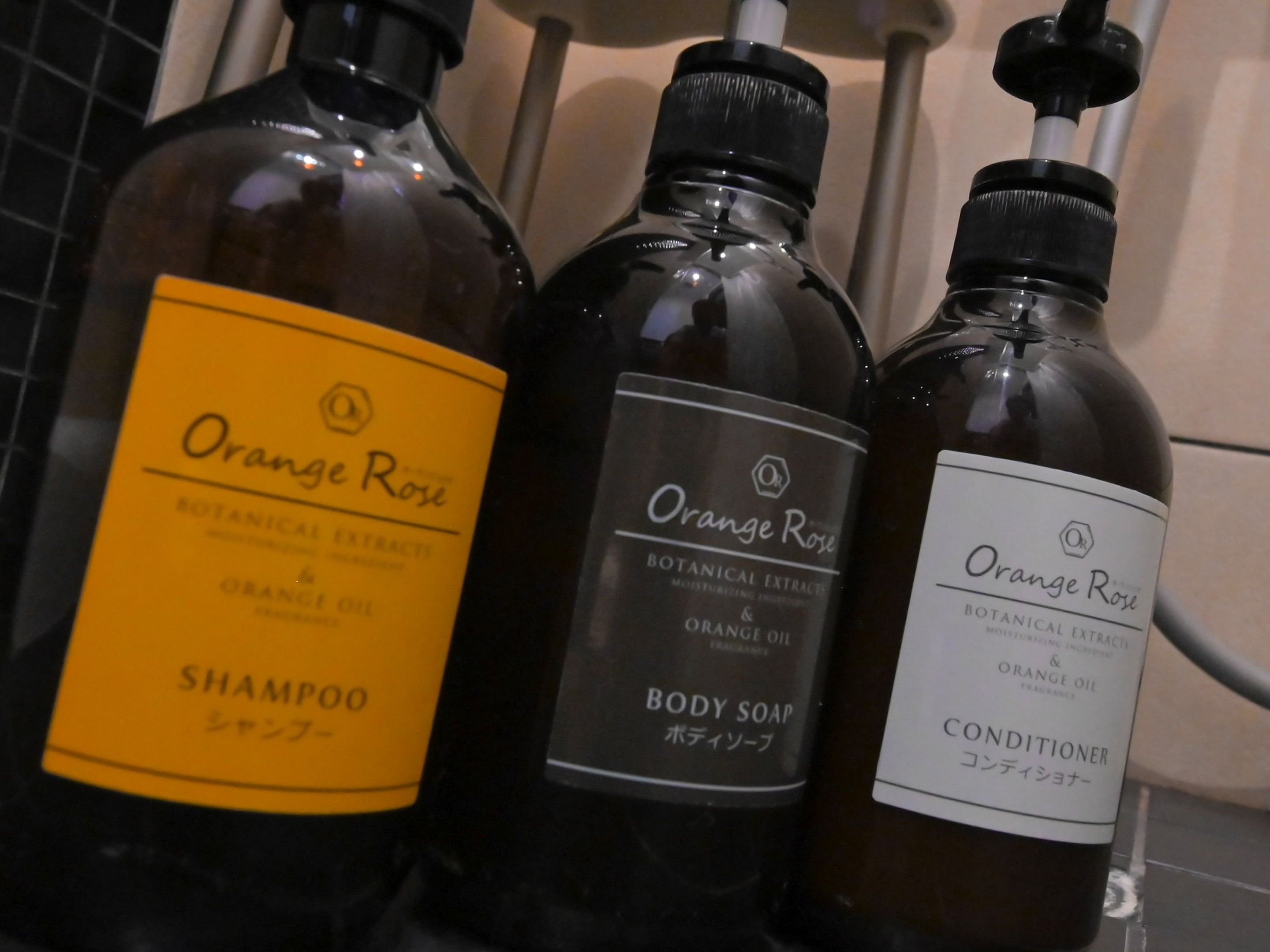Three bottles of Orange Rose products: a yellow shampoo, a black body soap, and a white conditioner.