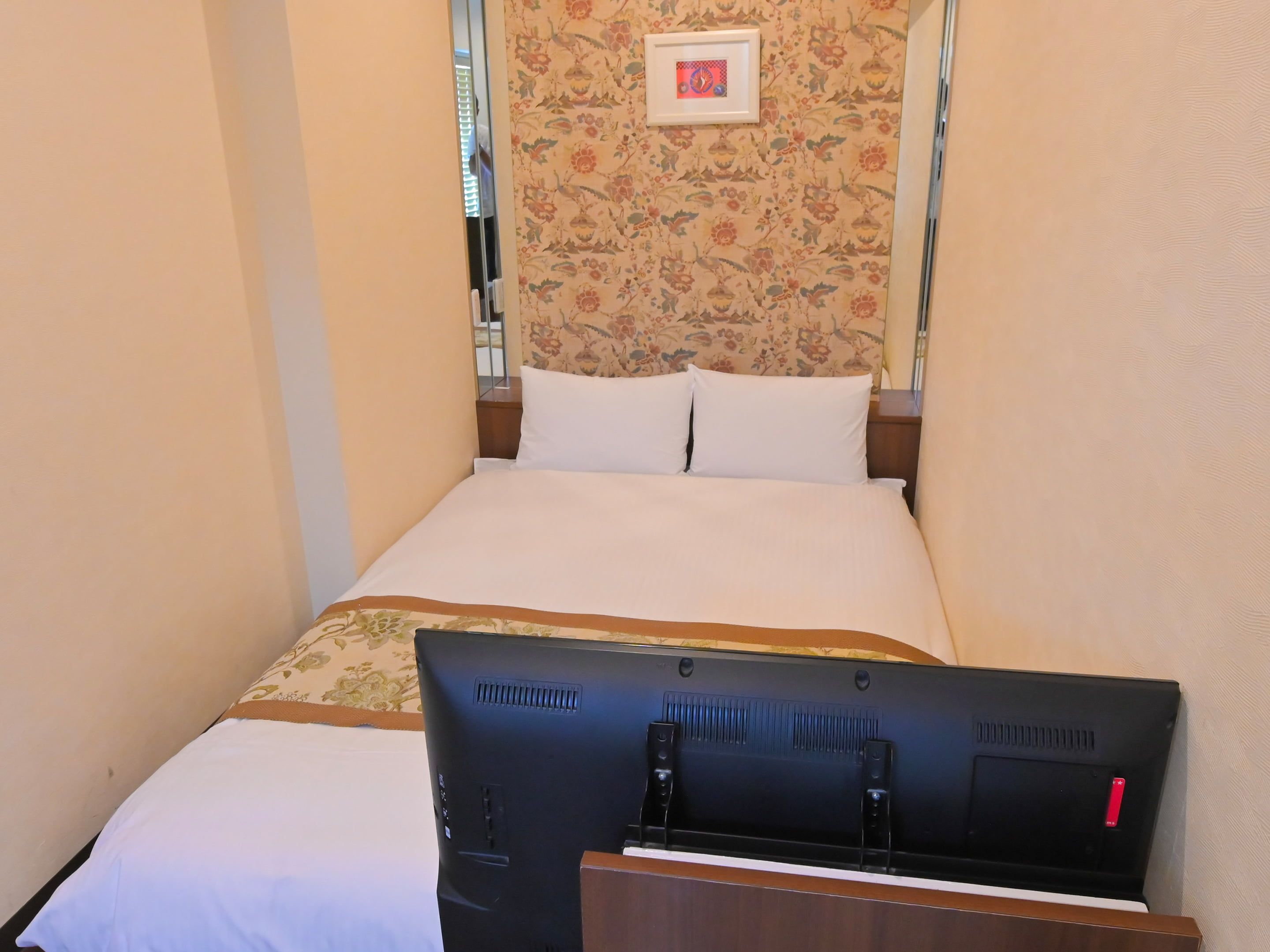 A hotel room with a bed, a flat-screen TV, and a floral-patterned wall.