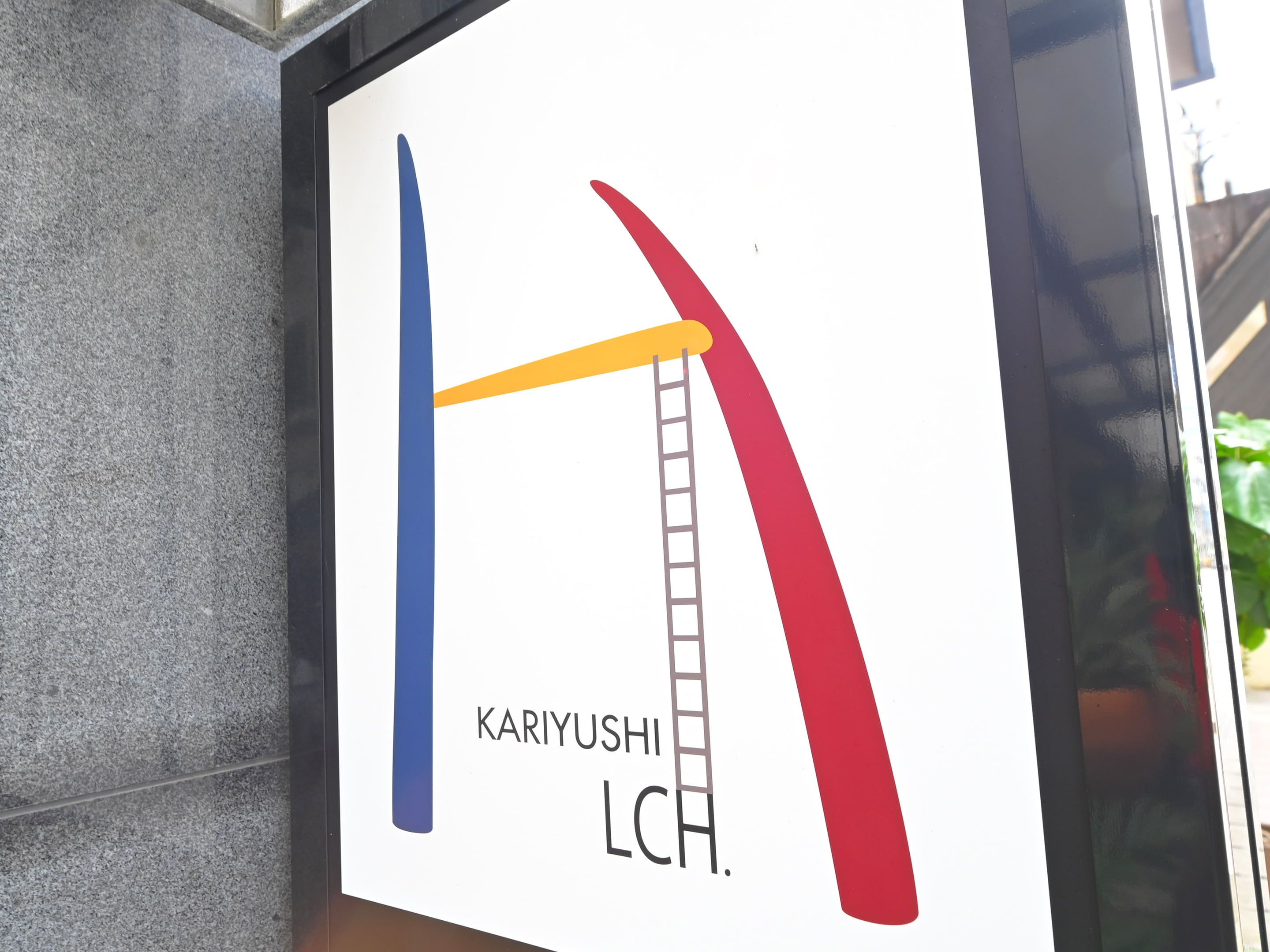 A sign with a blue and red curved line and a ladder, labeled 'KARIYUSHI LCH.'
