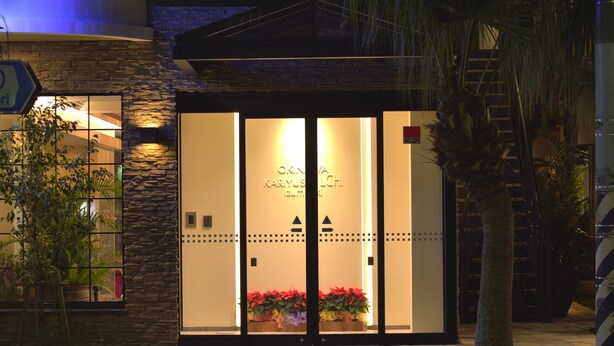 Entrada de un hotel con fachada de piedra, puertas de vidrio y un letrero que dice 'OKN KARYOS LCH'.