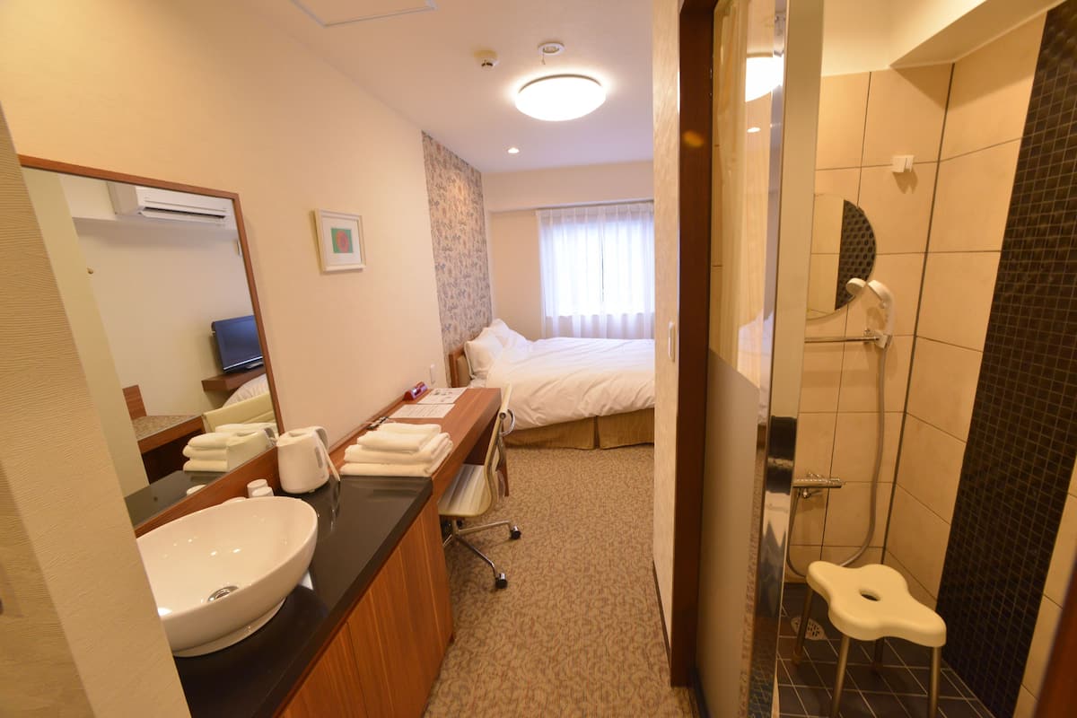 Ein Hotelzimmer mit einem großen Bett, einem Badezimmer mit Dusche, Waschbecken und Spiegel.